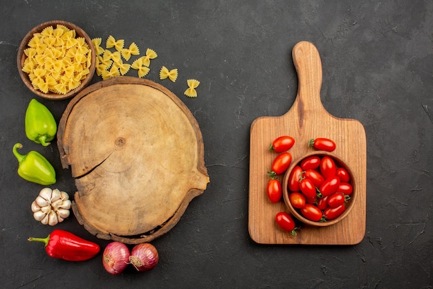 Top view appetizing vegetables bell pepper onion garlic pasta around the cutting board next to the bowl of tomatoes on the wooden board