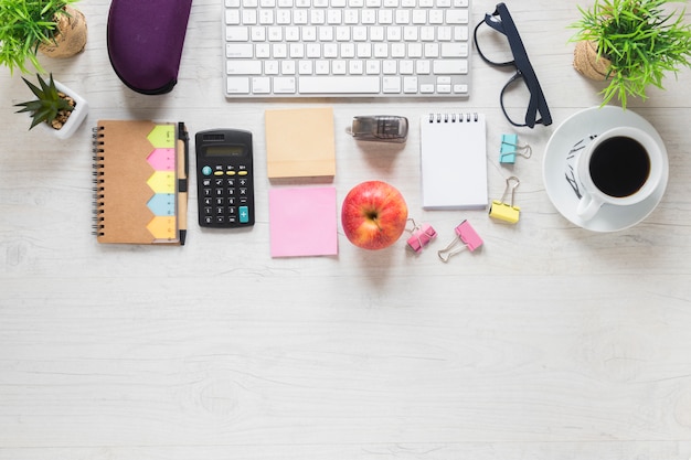 Top view of apple and coffee cup with office stationeries on white wooden desk