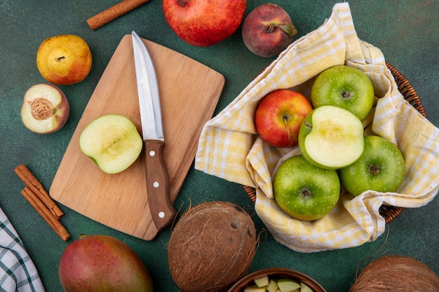 Вид сверху ломтика яблока на деревянной доске с ножом с разными яблоками и фруктами, такими как гранат, персик, груша на gre
