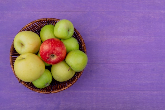 Top view of apples in basket on purple background with copy space