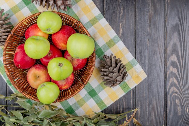 Top view of apples in basket with pinecones and leaves on plaid cloth and wooden background with copy space