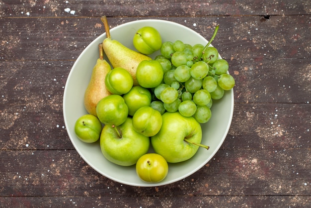 Вид сверху яблоки и виноград вместе с грушами и алычами внутри тарелки на деревянном деревенском фоне фруктовый сладкий мягкий витамин