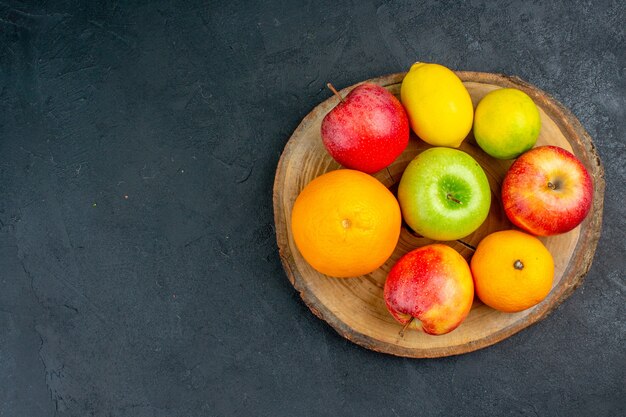 Top view apples lemon oranges on wood board on dark surface with copy space