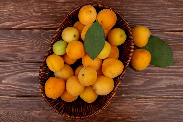 Top view of apricots in basket with leaves on wooden background