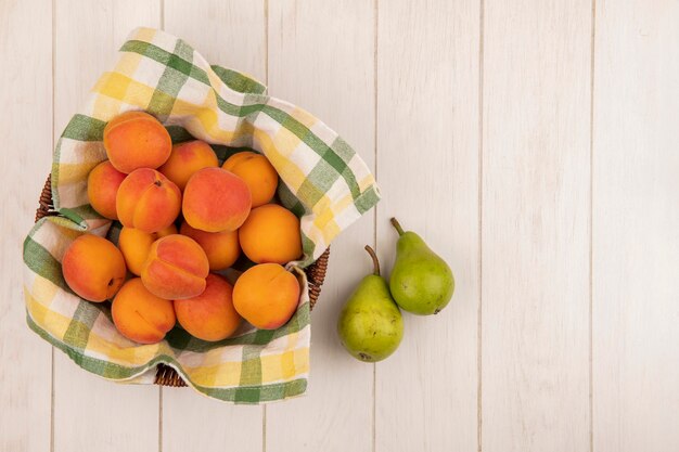 Top view of apricots in basket with pears on wooden background with copy space