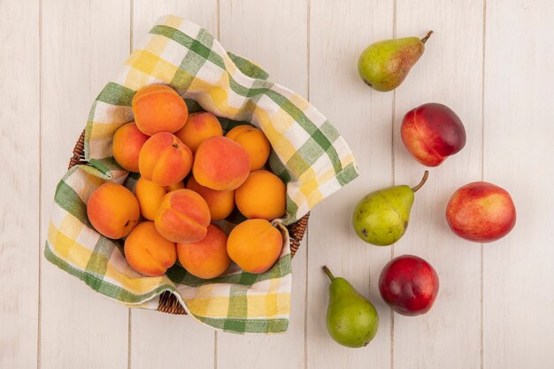Top view of apricots in basket with pears on wooden background