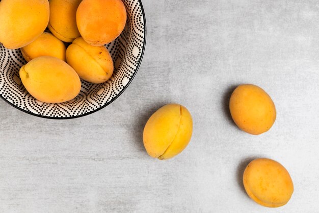 Top view of apricots in bowl on wooden background