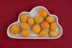 Free photo top view of apricots in a plate form a cloud on a red surface