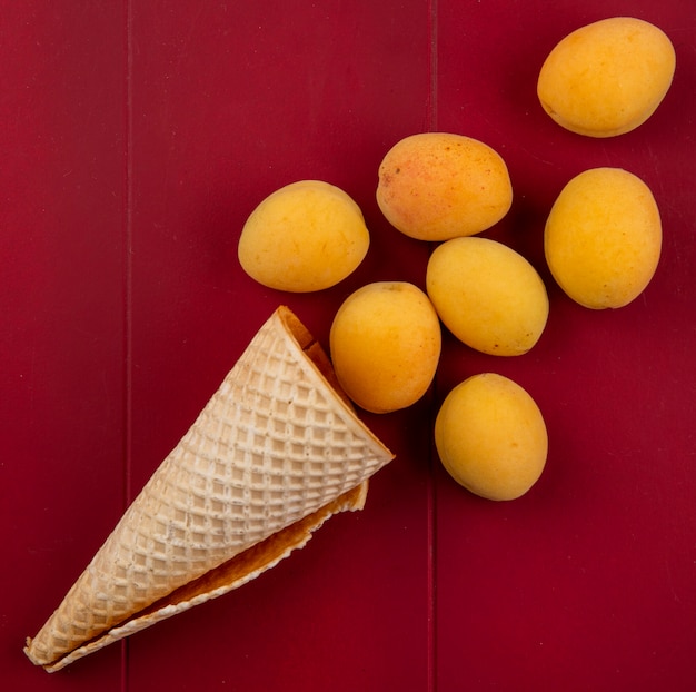 Top view of apricots with waffle cone on a red surface