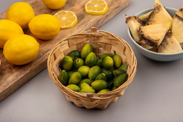 Top view of aromatic kinkans on a bucket with lemons on a wooden kitchen board on a grey background