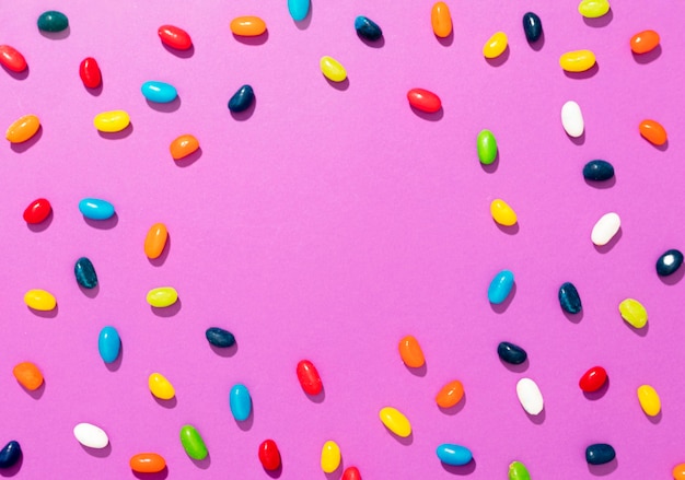 Top view arrangement of different colored candies on pink background with copy space
