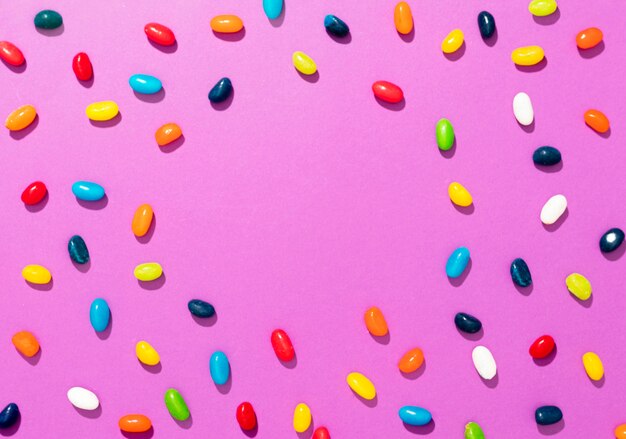 Вид сверху расположение разноцветных конфет на розовом фоне с копией пространства