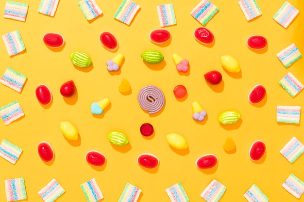 Вид сверху расположение разноцветных конфет на желтом фоне