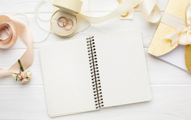 Top view arrangement of empty notebook and wedding rings