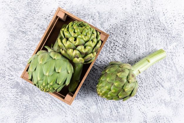 Top view artichokes in wooden box on light gray background. horizontal