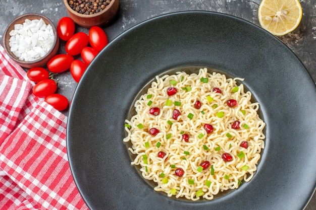 Foto gratuita vista dall'alto spaghetti ramen asiatici su piastra nera tagliati al limone pomodorini sale marino pepe nero in piccole ciotole sul tavolo scuro