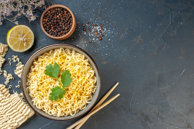 Top view asian ramen noodles in bowl black pepper in small bowl cut lemon chopsticks on dark table