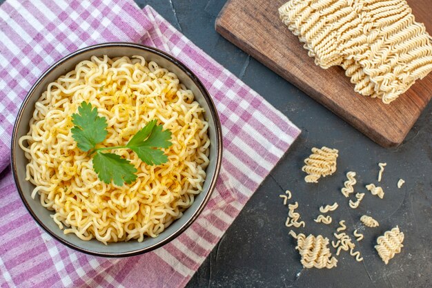 Top view asian ramen noodles in bowl on pink white checkered tablecloth raw ramen noodle on chopping board on dark background