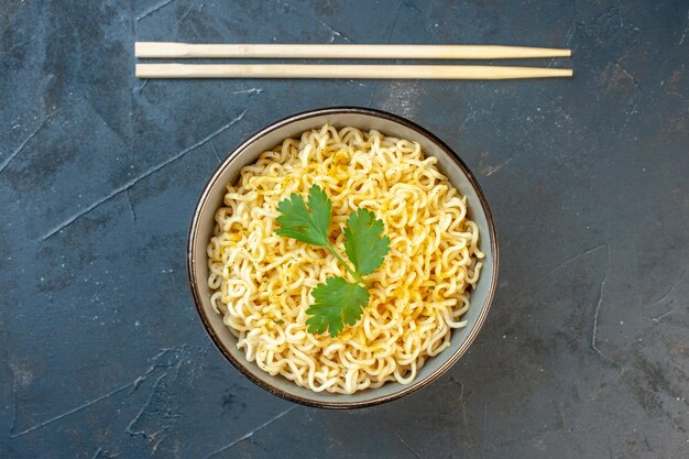 Top view asian ramen noodles with coriander in bowl chopsticks on dark table