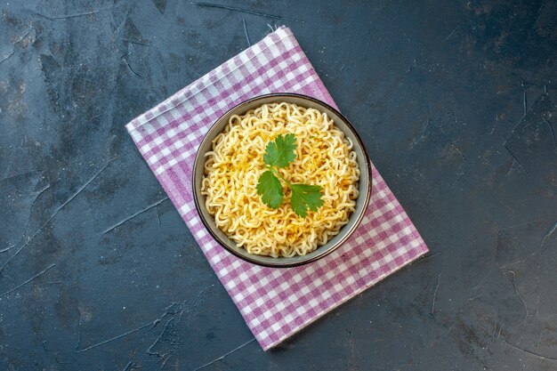 Top view asian ramen noodles with coriander in bowl on pink and white checkered kitchen towel on black table