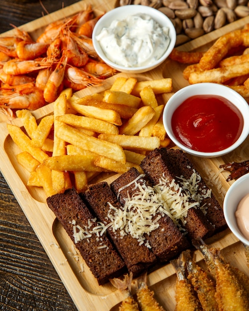 Top view of assorted beer snacks as fried bread sticks with cheese  french fries   pistachios and boiled shrimps with sauces on a wooden board