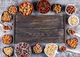 Free photo top view assorted nuts in mini different bowls with dark wooden board