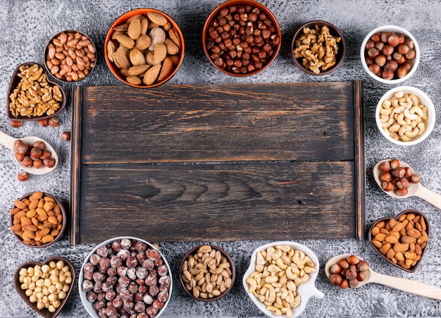 Top view assorted nuts in mini different bowls with dark wooden board