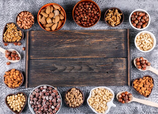 Top view assorted nuts in mini different bowls with dark wooden board