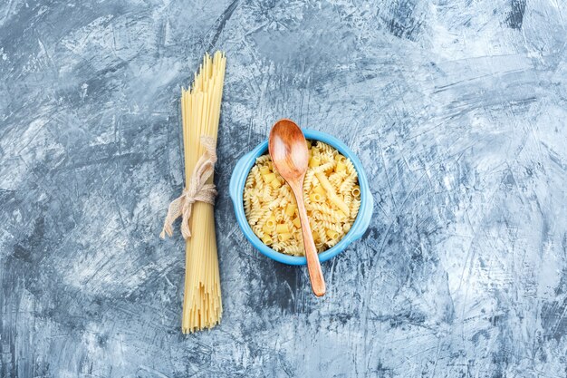 Top view assorted pasta in bowl with wooden spoon on grey plaster background. horizontal