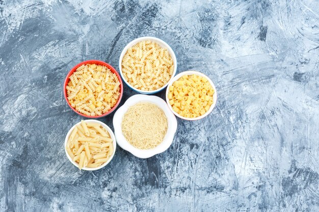 Top view assorted pasta in bowls on grey plaster background. horizontal