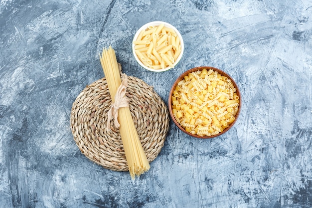 Top view assorted pasta in bowls on grey plaster and wicker placemat background. horizontal