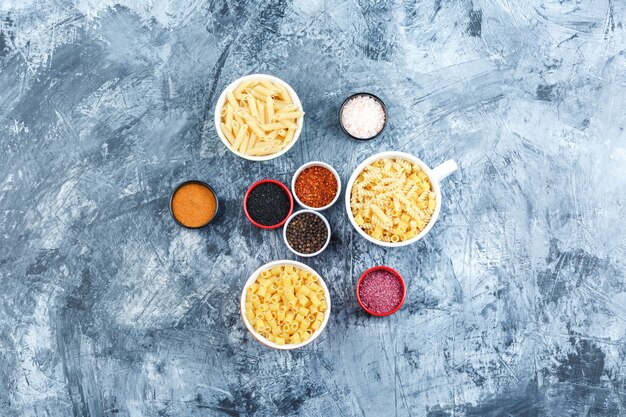 Top view assorted pasta in bowls with spices on grey plaster background. horizontal