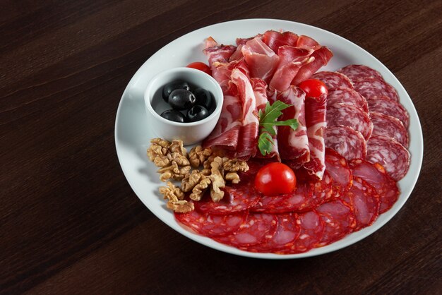 Top view of an assorted salami meat plate served with black olives and walnuts on the table