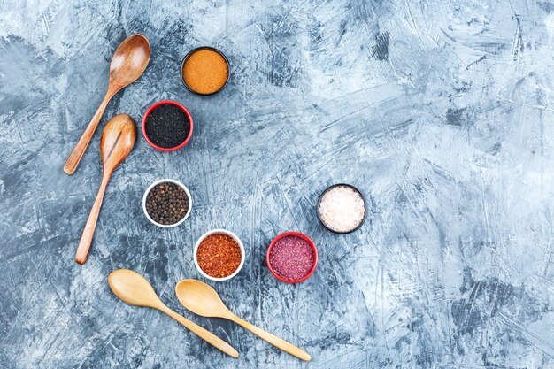 Top view assorted spices in small bowls with wooden spoons on grey plaster background. horizontal