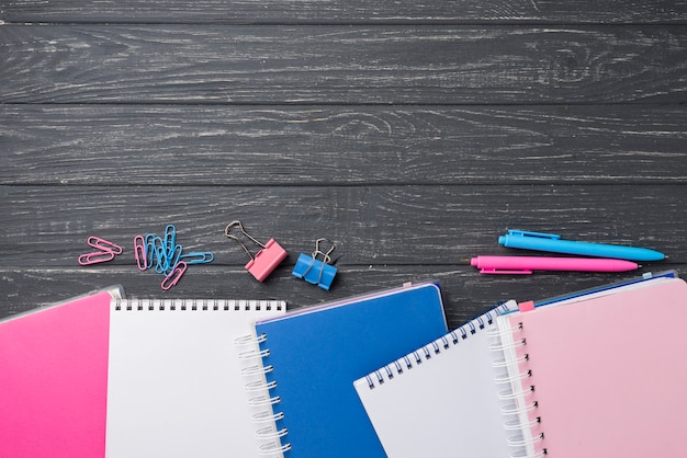 Top view of assortment on colored notebooks with pens and paper clips