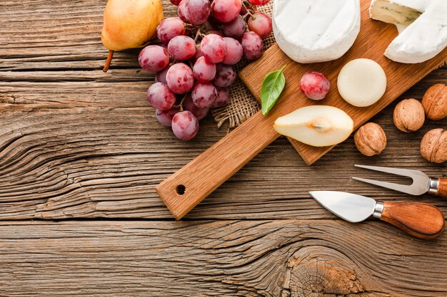 Top view assortment of gourmet cheese on wooden cutting board with grapes and ustensils