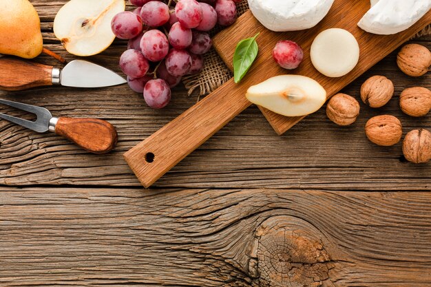 Top view assortment of gourmet cheese on wooden cutting board with grapes walnuts and ustensils