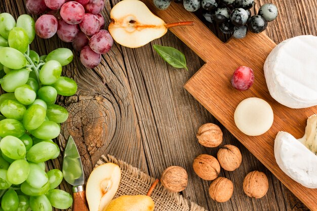 Top view assortment of gourmet cheese on wooden cutting board with grapes and walnuts