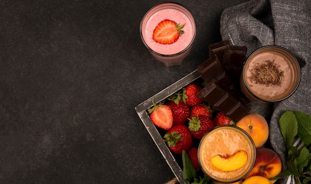 Top view of assortment of milkshake glasses on tray with fruits and chocolate