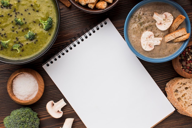 Top view of assortment of winter mushroom and broccoli soups with notebook