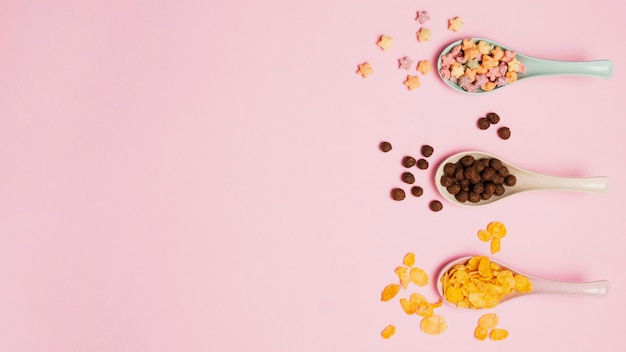 Top view assortment with spoons and cereals on pink background