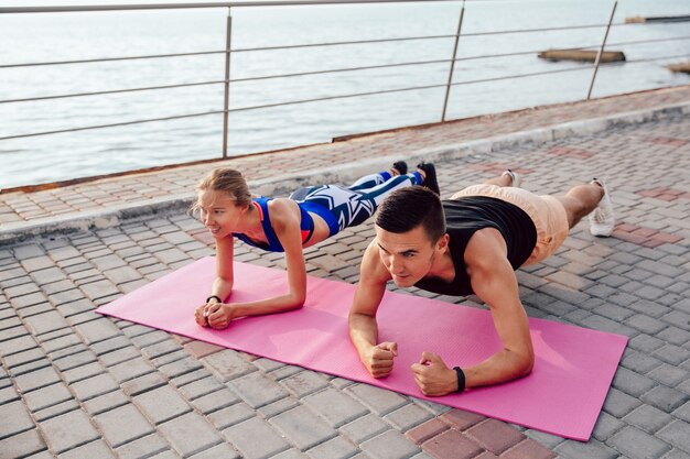 Top view of athlete sportive couple doing plank, training together on the quay
