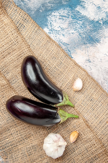 Free photo top view aubergines garlic on straw tablecloth on blue-white surface