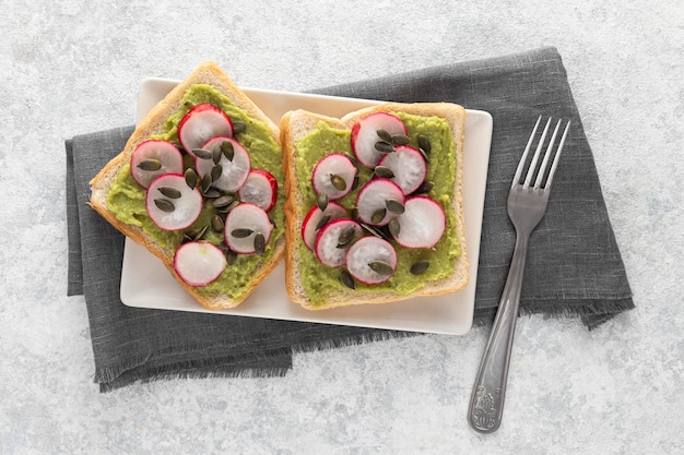 Free photo top view avocado toast with radish and seeds on plate with fork