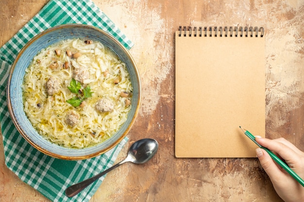 Foto gratuita vista dall'alto azero erishte in una ciotola su un asciugamano da cucina una penna verde in mano di una donna un quaderno su sfondo beige