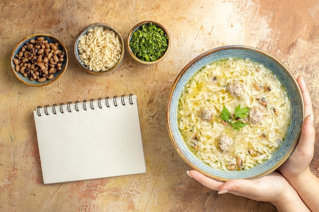 Top view azerbaijani erishte in bowl in woman hand notebook different stuffs in bowls on beige background