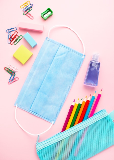 Top view of back to school stationery with colorful pencils and medical mask