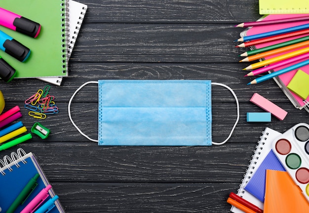 Top view of back to school stationery with face mask and colorful pencils