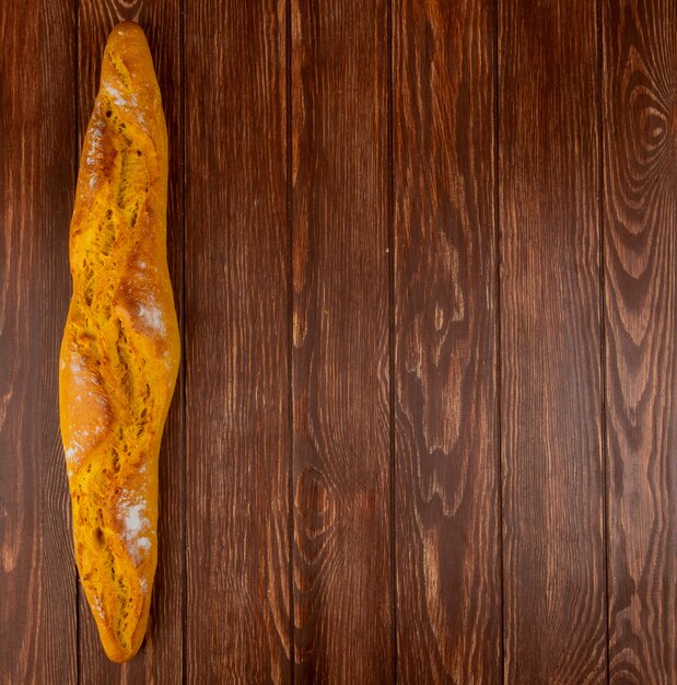 Top view of baguette on left side and wooden background with copy space