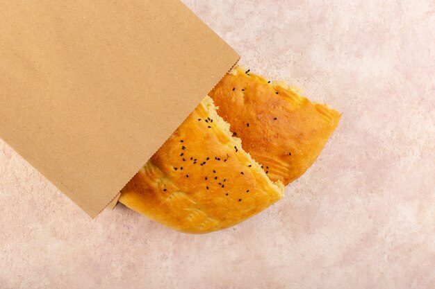 Вид сверху испеченный хлеб горячий вкусный свежий наполовину нарезанный внутри и снаружи бумажных пакетов на розовом